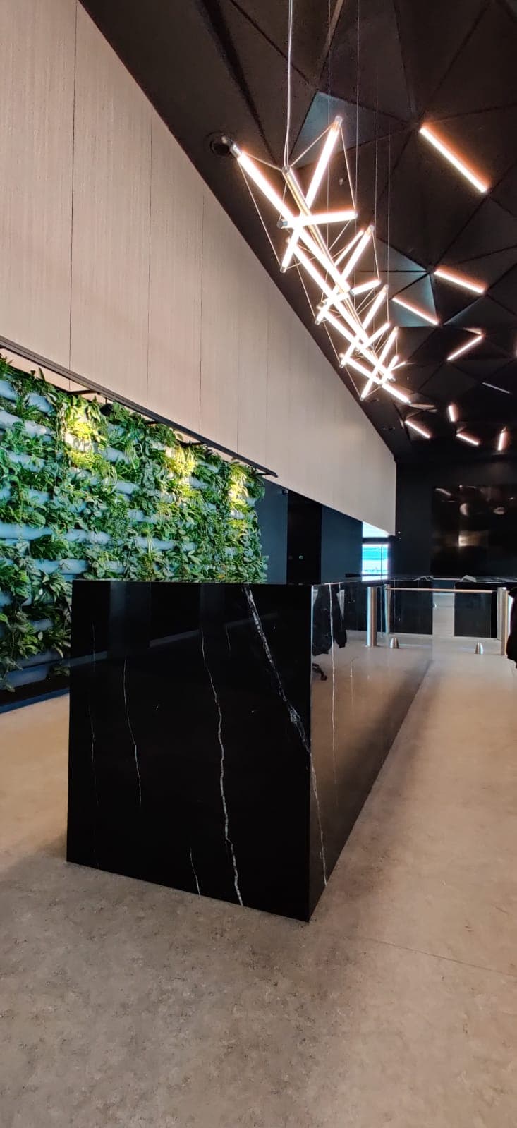 Recepție corporate cu birou monolit din marmură neagră lucioasă, perete vegetal iluminat și tavan negru cu structură geometrică fațetată.