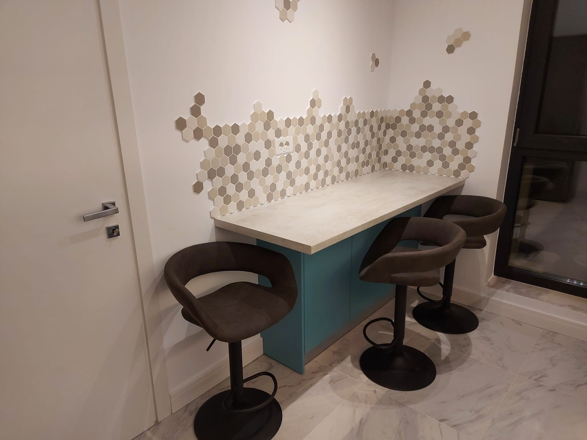 Colț de mic dejun cu bar cu blat în imitație de beton pe corp turcoaz, perete de accent din mozaic hexagonal și scaune de bar din catifea maro.